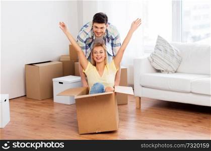 home, people, moving and real estate concept - happy couple having fun and riding in cardboard box at new home. happy couple having fun with boxes at new home