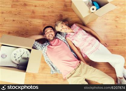 home, people, repair and real estate concept - happy couple with cardboard boxes and stuff lying on floor to new place