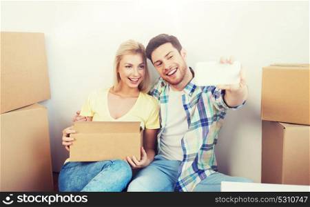home, people, repair and real estate concept - smiling couple with big cardboard boxes moving to new place and taking smartphone selfie. couple with taking smartphone selfie and moving