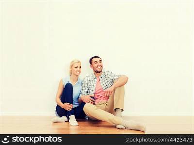 home, people, repair, moving and real estate concept - happy couple of man and woman sitting on floor and dreaming at new place