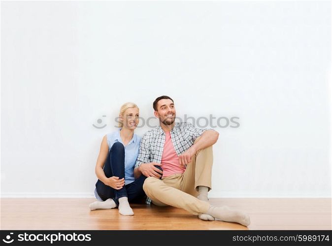 home, people, repair, moving and real estate concept - happy couple of man and woman sitting on floor and dreaming at new place
