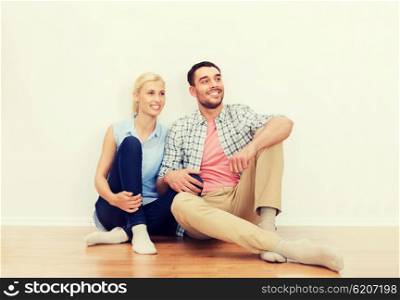 home, people, repair, moving and real estate concept - happy couple of man and woman sitting on floor at new place