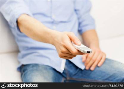 home, people, technology and entertainment concept - close up of man changing channels with tv remote control at home