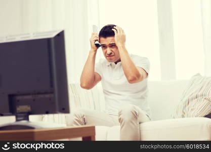 home, people, technology and entertainment concept - disappointed man watching sports on tv and supporting team at home