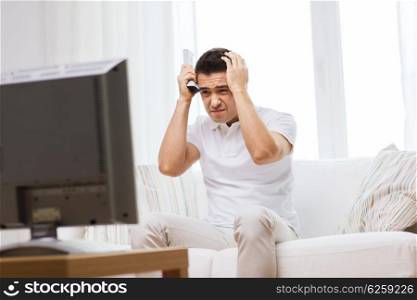 home, people, technology and entertainment concept - disappointed man watching sports on tv and supporting team at home