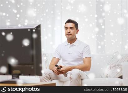 home, people, technology and entertainment concept - man with remote control watching tv at home over snow effect