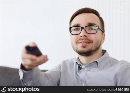 home, people, technology and entertainment concept - smiling man in eyeglasses with tv remote control at home