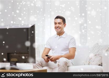 home, people, technology and entertainment concept - smiling man with remote control watching tv at home over snow effect
