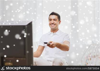 home, people, technology and entertainment concept - smiling man with remote control watching tv at home over snow effect