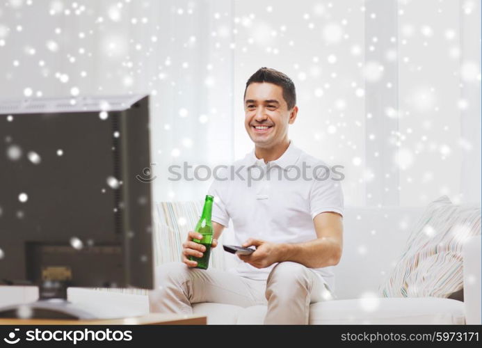 home, people, technology and entertainment concept - smiling man with remote control watching tv and drinking beer at home over snow effect