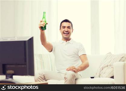 home, people, technology and entertainment concept - smiling man with remote control watching tv and drinking beer at home