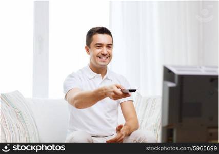 home, people, technology and entertainment concept - smiling man with remote control watching tv at home