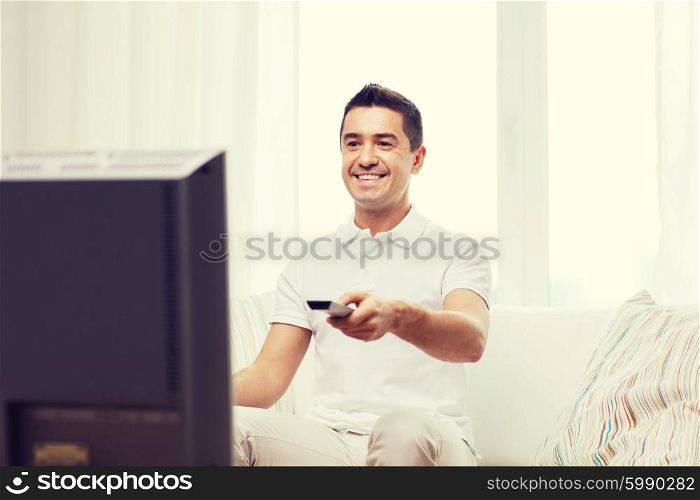 home, people, technology and entertainment concept - smiling man with remote control watching tv at home