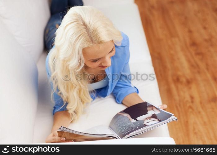 home, reading and leisure concept - smiling woman lying on couch and reading magazine at home