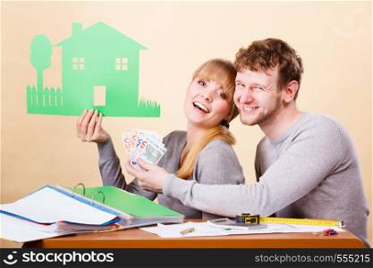 Home real estate credit mortgage concept. Couple with house and money. Young man and woman counting banknotes and holding cartboard cutout.. Couple with house and money.