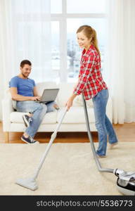home, relations and cleaning concept - smiling woman with hoover and young man with laptop at home