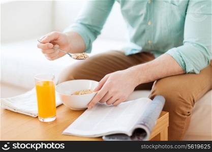 home, rest, news, breakfast and people concept - close up of man reading magazine and eating breakfast at home