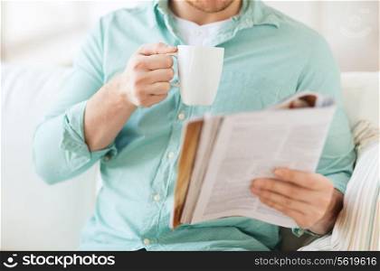 home, rest, news, drinks and people concept - close up of man reading magazine and drinking from cup sitting on couch at home