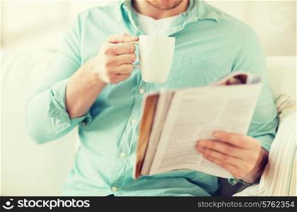 home, rest, news, drinks and people concept - close up of man reading magazine and drinking from cup sitting on couch at home