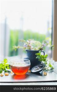 Home scene with Cup of hot herbal tea on window still at nature background, vertical. Healthy drinks, detox or clean food concept