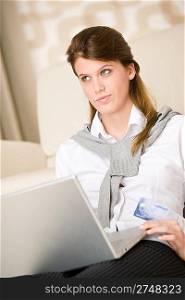 Home shopping - woman with credit card and laptop in lounge thinking