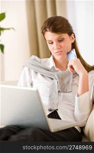 Home shopping - woman with credit card and laptop in lounge thinking