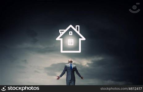 Home symbol. Businessman with hands spread apart and house model above
