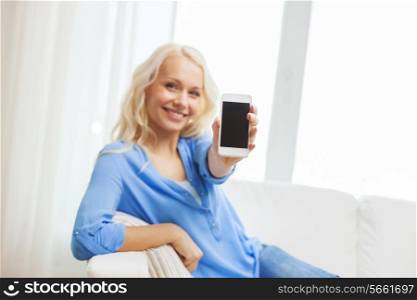 home, technology, advertising and internet concept - smiling woman with showing blank smartphone screen sitting on couch at home