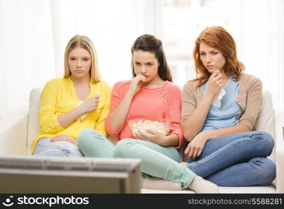 home, technology and friendship concept - three sad teenage girl watching tv at home and eating popcorn