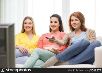 home, technology and friendship concept - three smiling teenage girl watching tv at home and eating popcorn