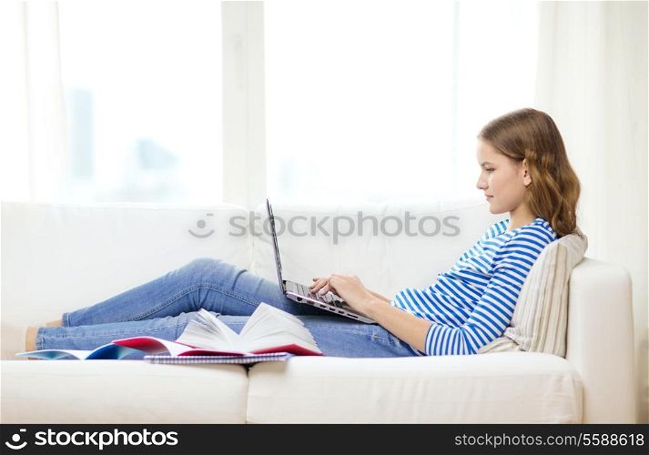 home, technology and internet concept - busy teenage girl lying on the couch with laptop computer at home