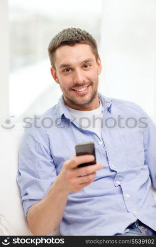 home, technology and internet concept - smiling man with smartphone sitting on couch at home