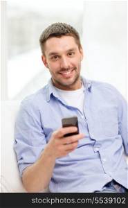 home, technology and internet concept - smiling man with smartphone sitting on couch at home