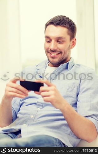 home, technology and internet concept - smiling man with smartphone sitting on couch at home