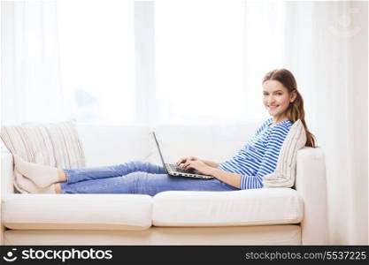 home, technology and internet concept - smiling teenage girl lying on the couch with laptop computer at home