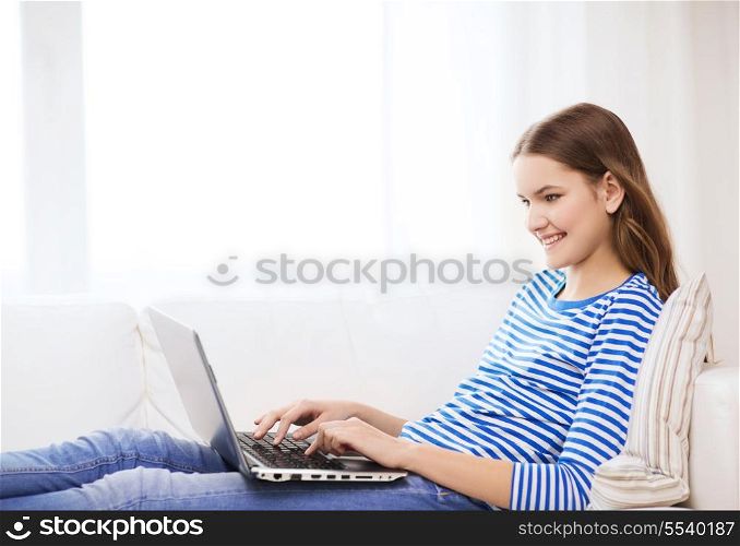 home, technology and internet concept - smiling teenage girl lying on the couch with laptop computer at home