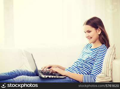 home, technology and internet concept - smiling teenage girl lying on the couch with laptop computer at home