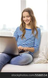 home, technology and internet concept - smiling teenage girl sitting on the couch with laptop computer at home