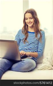 home, technology and internet concept - smiling teenage girl sitting on the couch with laptop computer at home