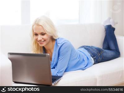 home, technology and internet concept - smiling woman lying on the couch with laptop computer at home