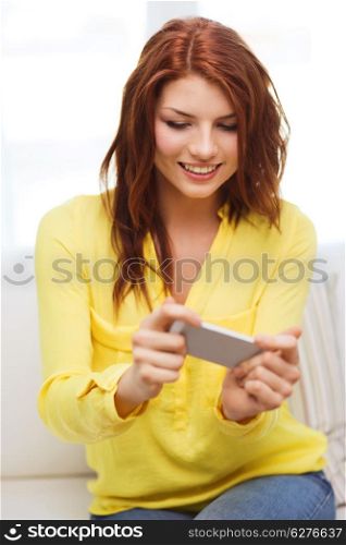 home, technology and internet concept - smiling woman playing with smartphone sitting on couch at home