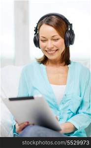 home, technology and internet concept - smiling woman sitting on the couch with tablet pc conputer and headphones at home