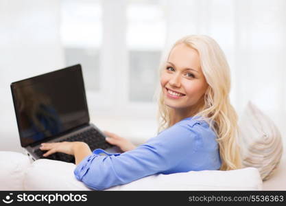 home, technology and internet concept - smiling woman sitting on the couch with laptop computer at home