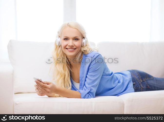 home, technology and internet concept - smiling woman with smartphone and headphones lying on couch at home