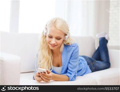 home, technology and internet concept - smiling woman with smartphone and headphones lying on couch at home