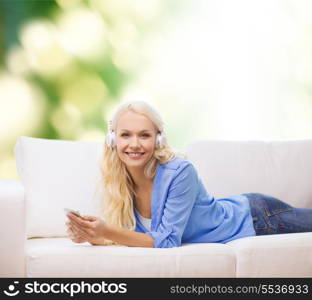 home, technology and internet concept - smiling woman with smartphone and headphones lying on couch outdoors