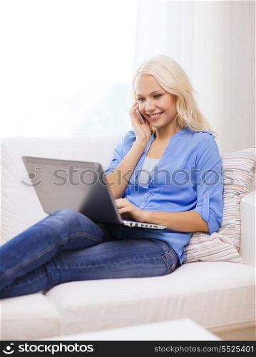 home, technology and internet concept - smiling woman with smartphone and laptop computer sitting on couch at home