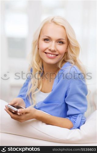 home, technology and internet concept - smiling woman with smartphone lying on couch at home