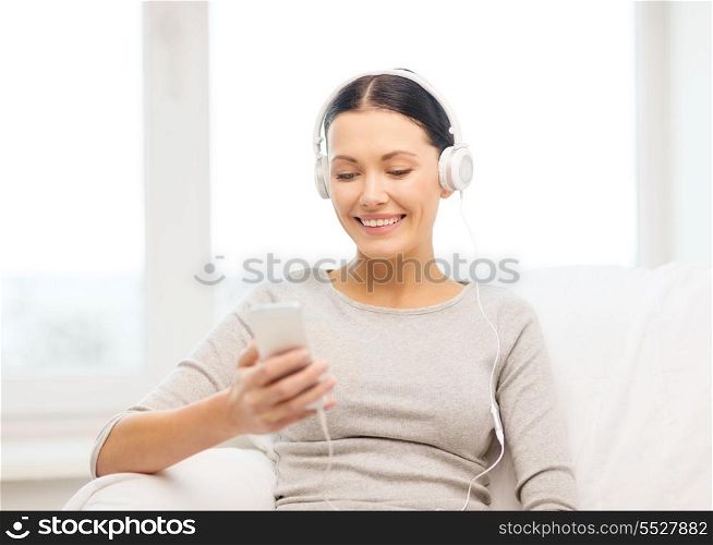 home, technology, communication and internet concept - woman sitting on the couch with smartphone and headphones at home