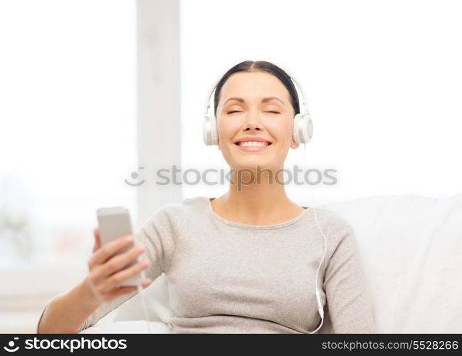 home, technology, communication and internet concept - woman sitting on the couch with smartphone and headphones at home